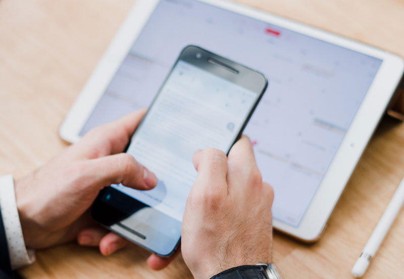 hands holding a phone with a tablet in the background